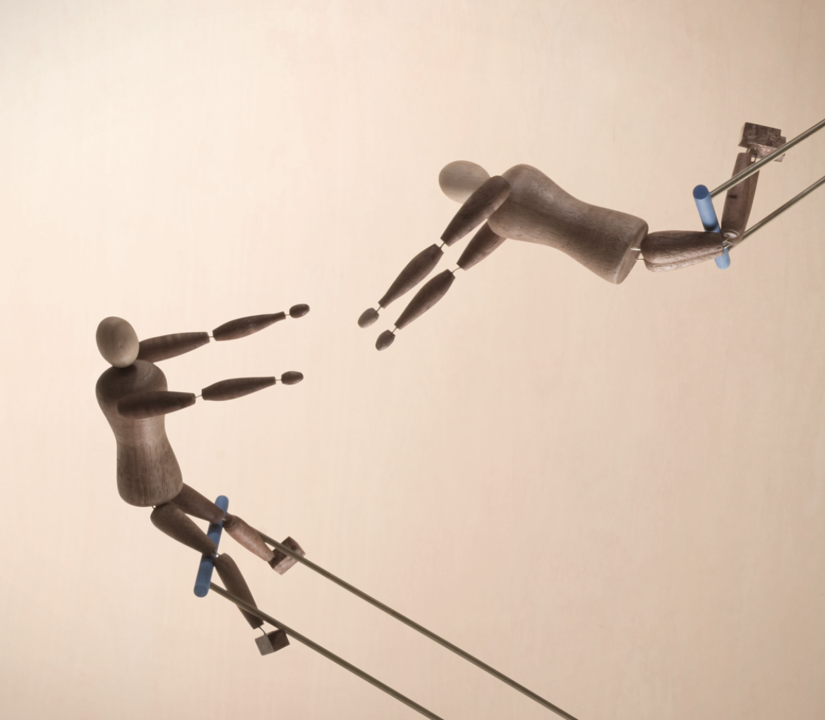 Zwei Holzpuppen hängen an Fäden und scheinen in entgegengesetzte Richtungen zu schwingen.